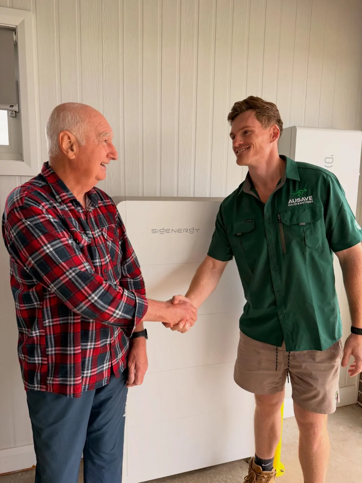 An Ausave installer shaking hands with a homeowner beside a Sigenergy battery